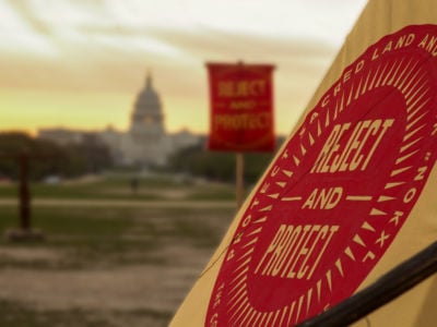 A red sign in front of the Capitol that says "Protect sacred lands and water #NoKXL" and "Reject and Protect"