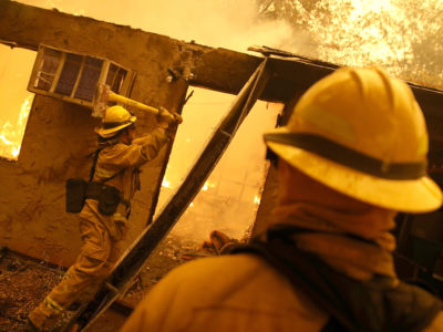 Firefighters try to keep flames from a burning home from spreading to a neighboring apartment complex as they battle the Camp Fire on November 9, 2018, in Paradise, California.
