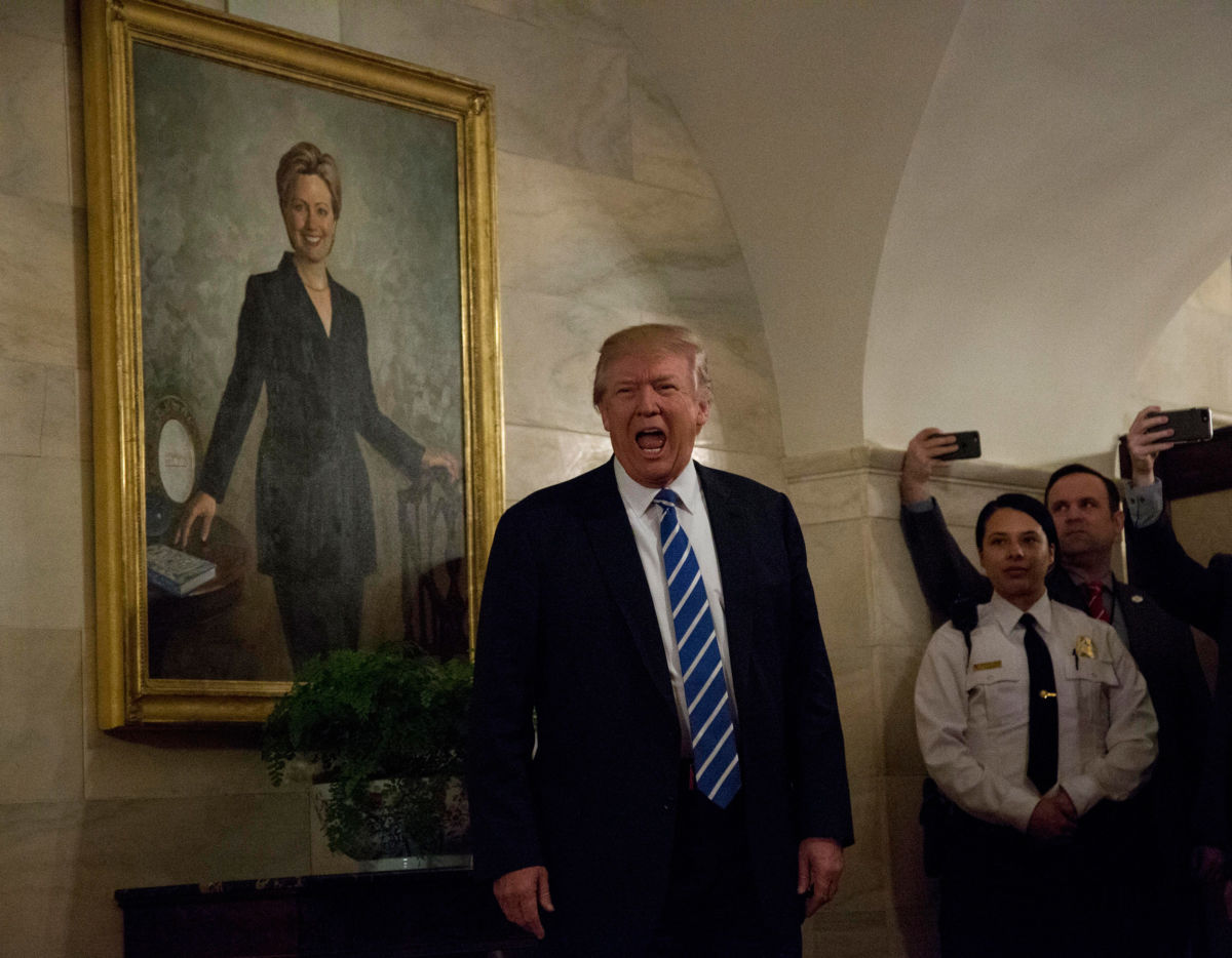 President Trump walks in a corridor of the White House to greet visitors, while a portrait of Hillary Clinton hangs on the wall, March 7, 2017, in Washington, DC.