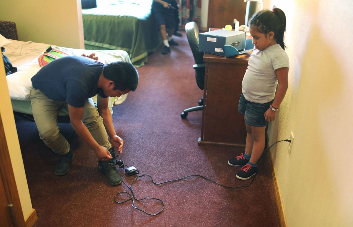 A young girl watches as her father plugs in his ankle monitor for charging at an Annunciation House facility after being reunited with each other on July 25, 2018, in El Paso, Texas. Originally from Guatemala, the two were separated for about two months after attempting to cross into the US.