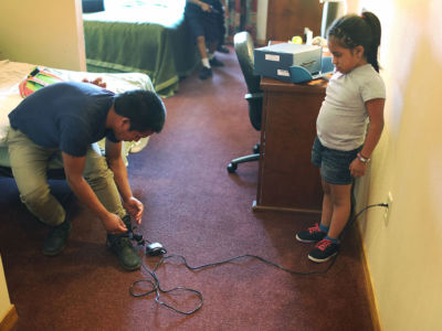 A young girl watches as her father plugs in his ankle monitor for charging at an Annunciation House facility after being reunited with each other on July 25, 2018, in El Paso, Texas. Originally from Guatemala, the two were separated for about two months after attempting to cross into the US.