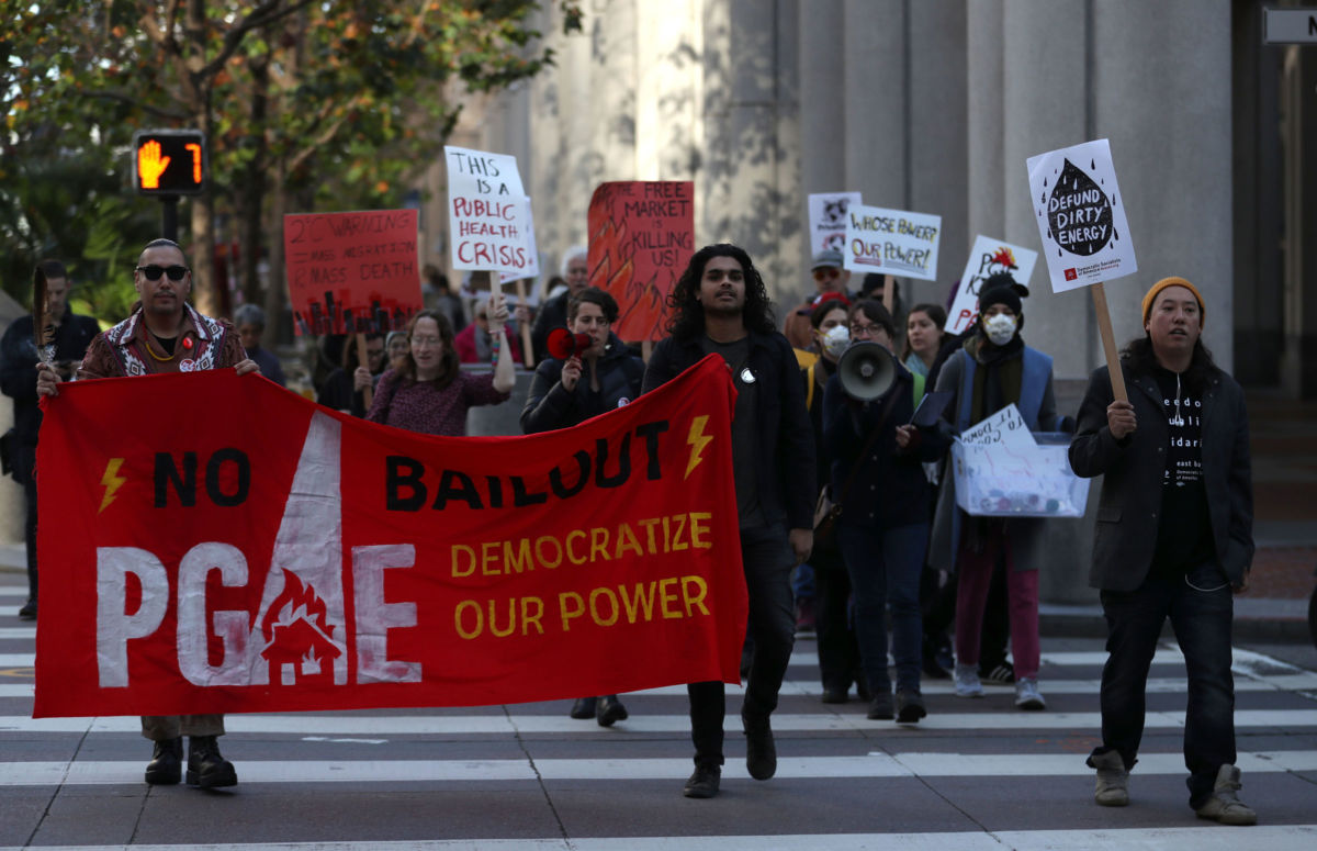 Protesters hold signs as they march to the Pacific Gas and Electric (PG&E) headquarters on December 11, 2018, in San Francisco, California. More than two dozen protesters staged a demonstration inside the lobby of the PG&E headquarters to demand that the energy company be held accountable for the Camp Fire that killed 85 people and destroyed over 18,000 structures in and around Paradise, California, last year.