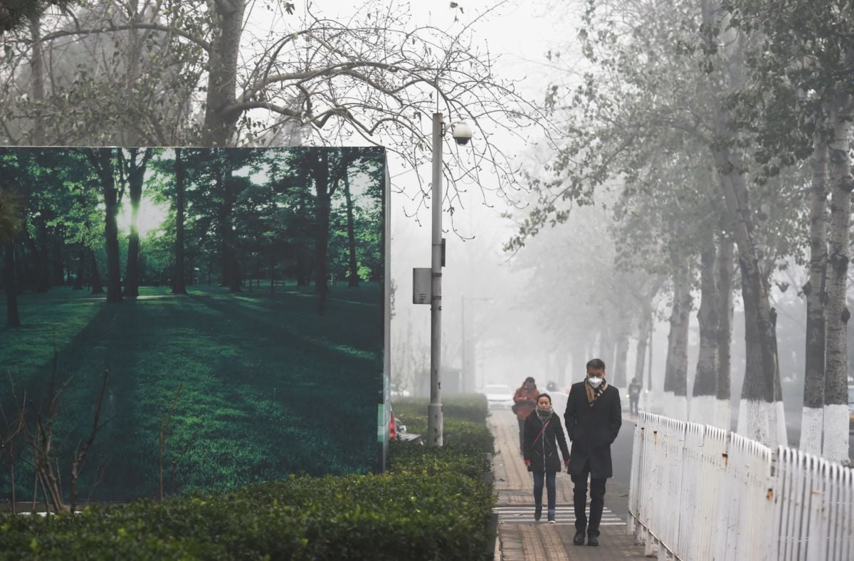 Pedestrians walk past a billboard scene of green trees and grass on a heavily polluted day in Beijing, China, on December 1, 2015.