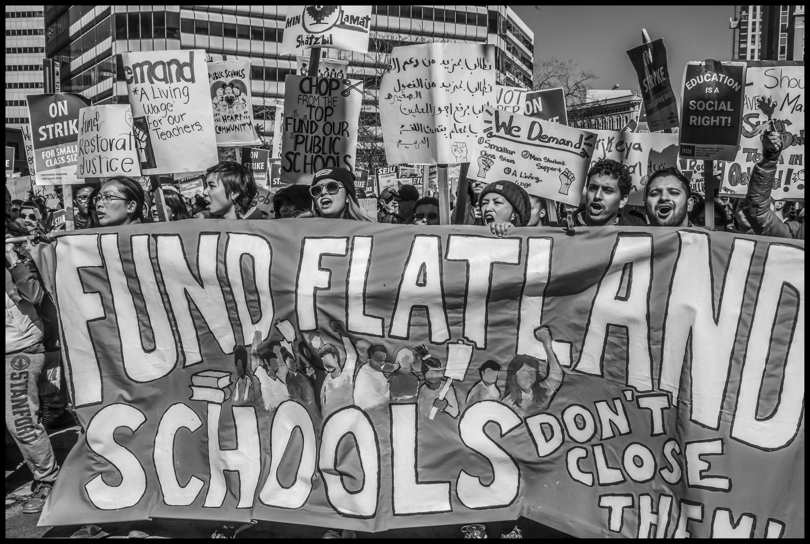 Teachers and community members march behind a banner opposing the closure of 24 schools, which targets schools in the Oakland flatlands, predominantly low-income communities of color.