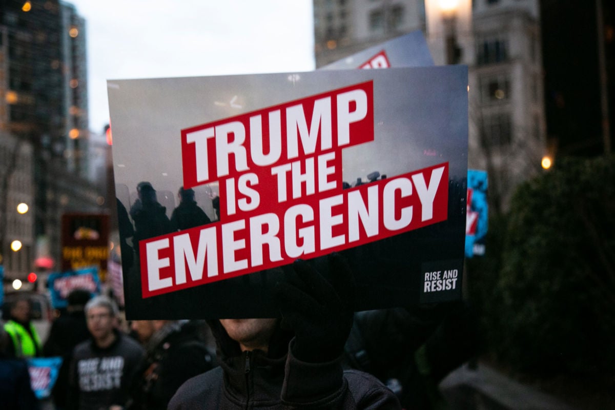 A person holds protest sign that reads "Trump is the emergency" in front of Trump International Hotel on February 15, 2019, in New York City. The group is protesting President Donald Trump's declaration of a National Emergency in order to build his proposed border wall.