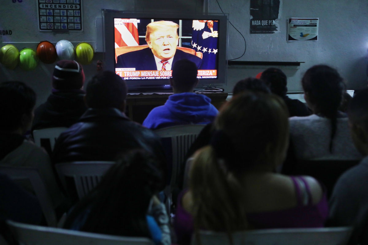 Migrants view a live televised speech by President Donald Trump on border security at a shelter for migrants on January 8, 2019, in Tijuana, Mexico.