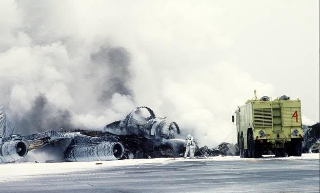 A crash crewman sprays a foam/water agent on an Alaska Air National Guard KC-135E Stratotanker aircraft that exploded and burned while taxiing to a parking area.