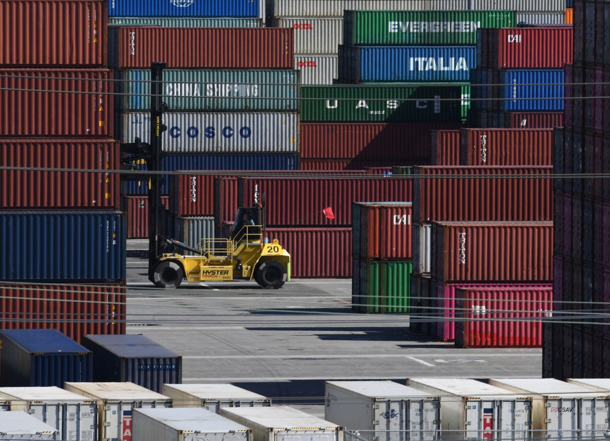 shipping containers are stacked high as they're unloaded by a forklift