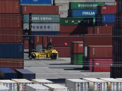 shipping containers are stacked high as they're unloaded by a forklift