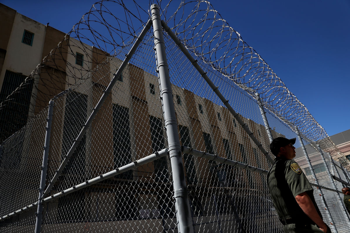 Officer stands in front of fence surrounding prison building