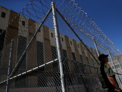 Officer stands in front of fence surrounding prison building