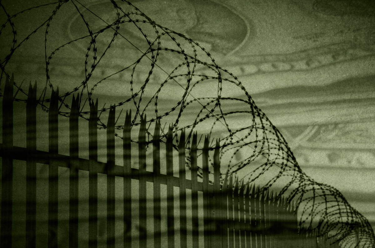 A barbed wire prison fence with U.S. currency overlay