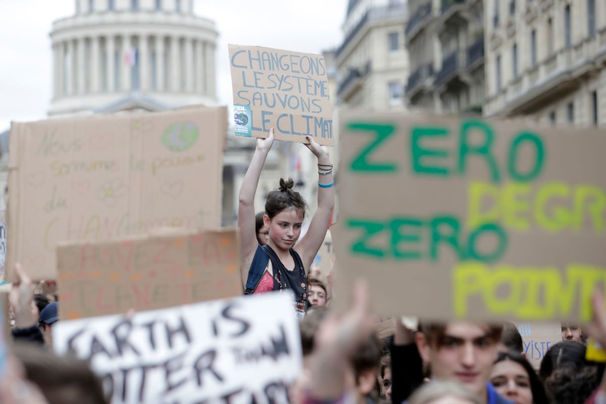 A young woman holds a sign reading "Change the system, not the climate" in French amidst a crowd of prosters