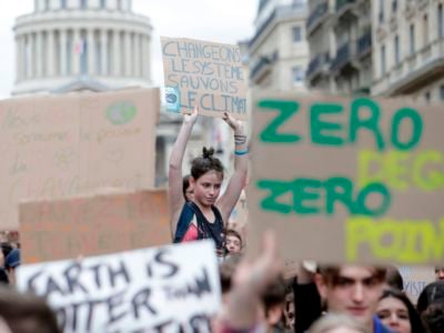 A young woman holds a sign reading "Change the system, not the climate" in French amidst a crowd of prosters