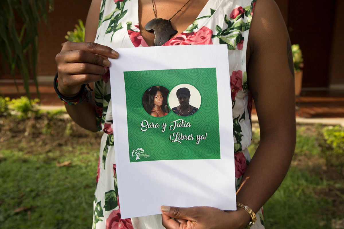 A participant at the February conference holds a sign featuring Sara Quiñonez's and Tulia Maris Valencia's photos.