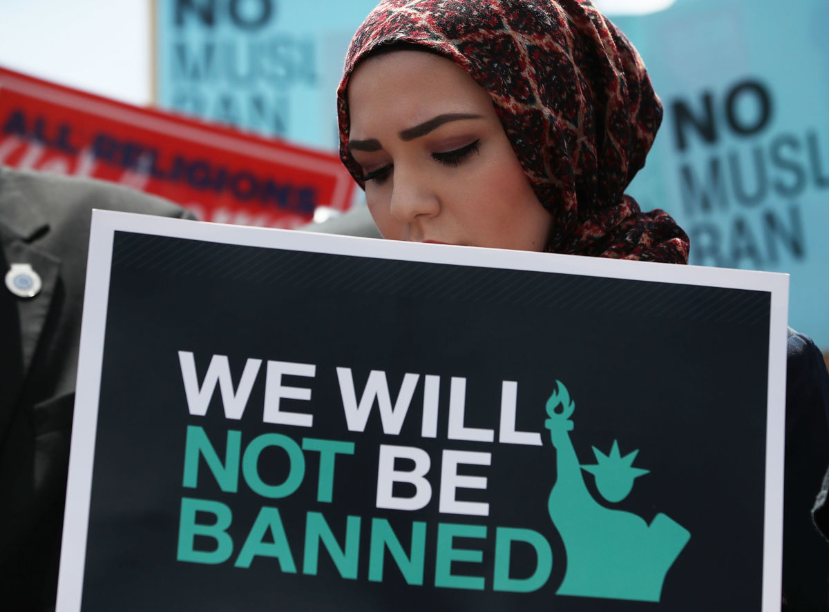 A hijabi holds a sign that displays the statue of liberty and reads "We will not be banned"