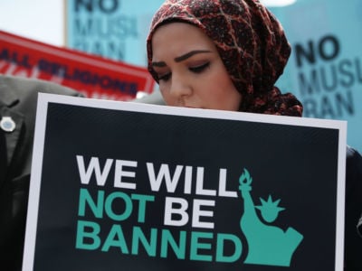 A hijabi holds a sign that displays the statue of liberty and reads "We will not be banned"