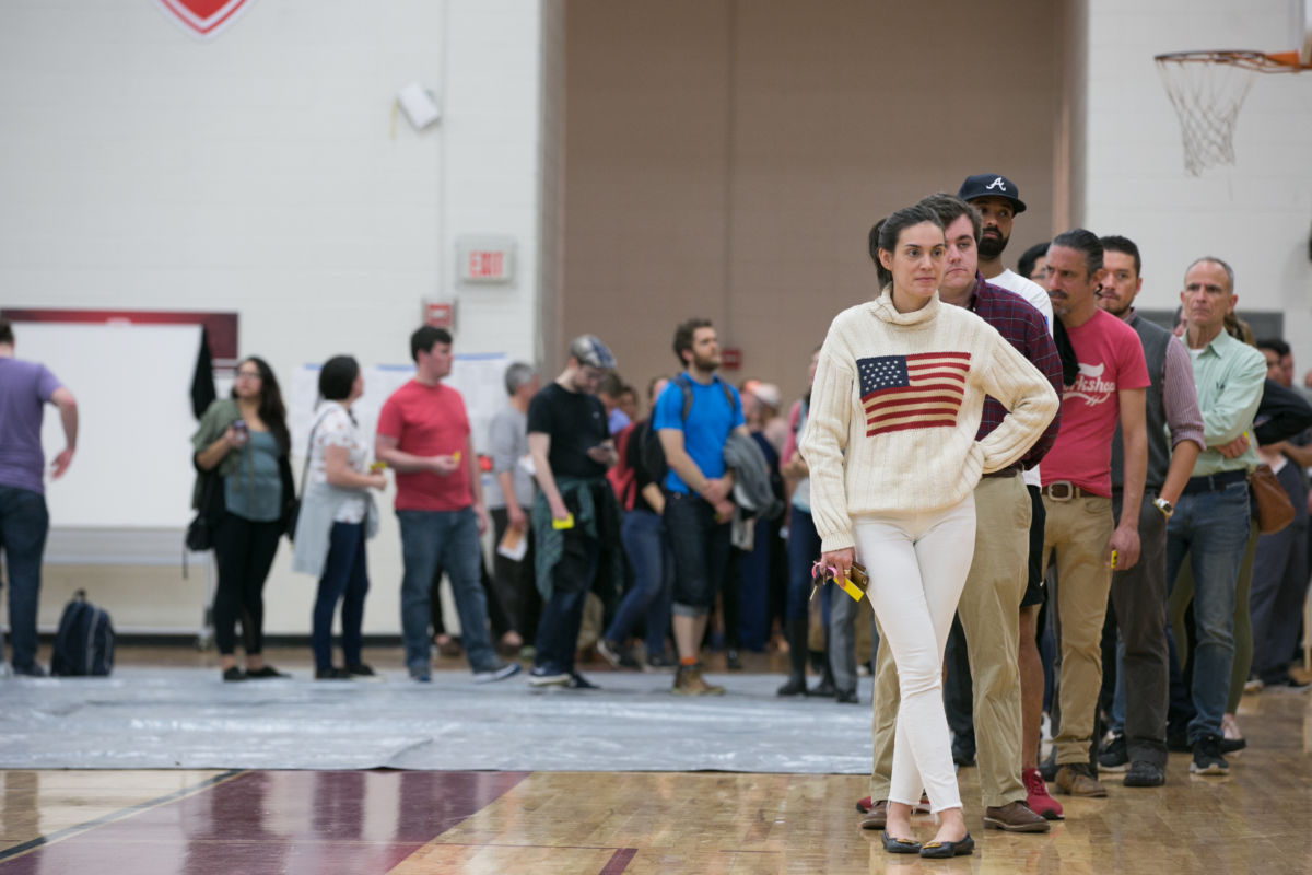 Woman in a US flag sweater stands at the front of a long line of waiting voters