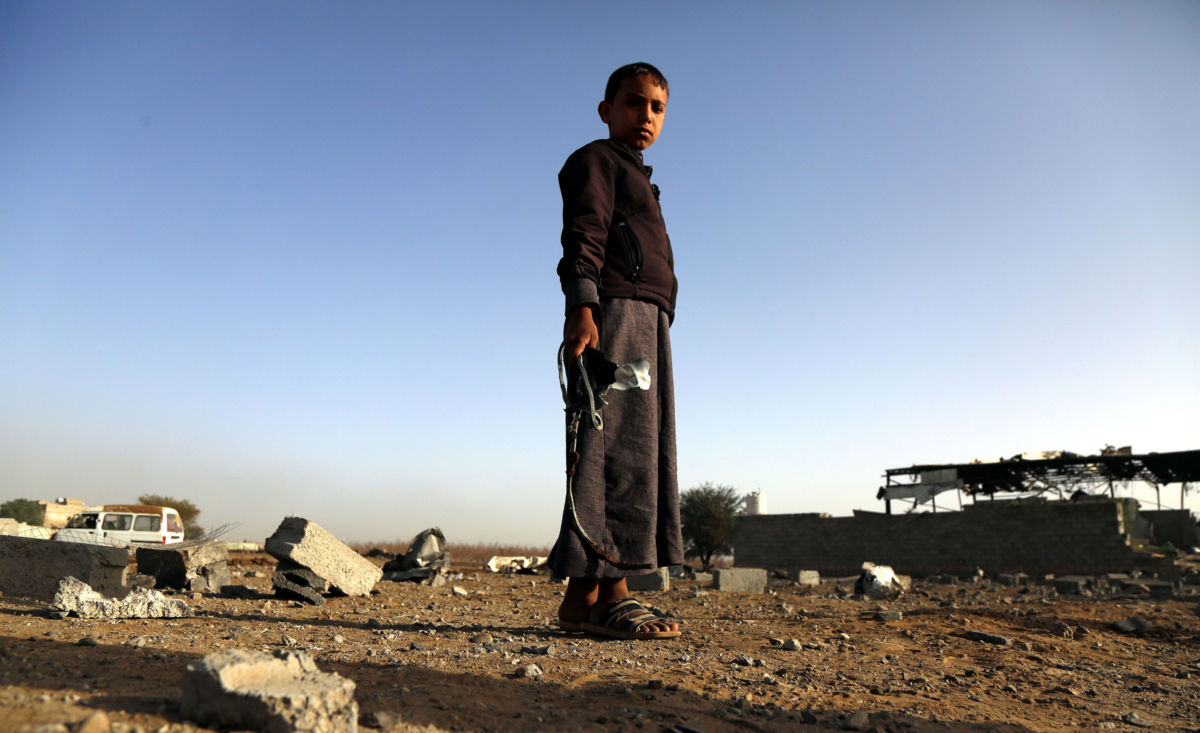 A Yemeni child holds missile shrapnel outside factory destroyed by airstrikes.