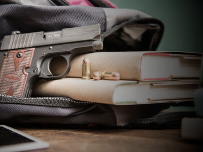 A gun sticks out of a backpack on a school desk with textbooks nearby