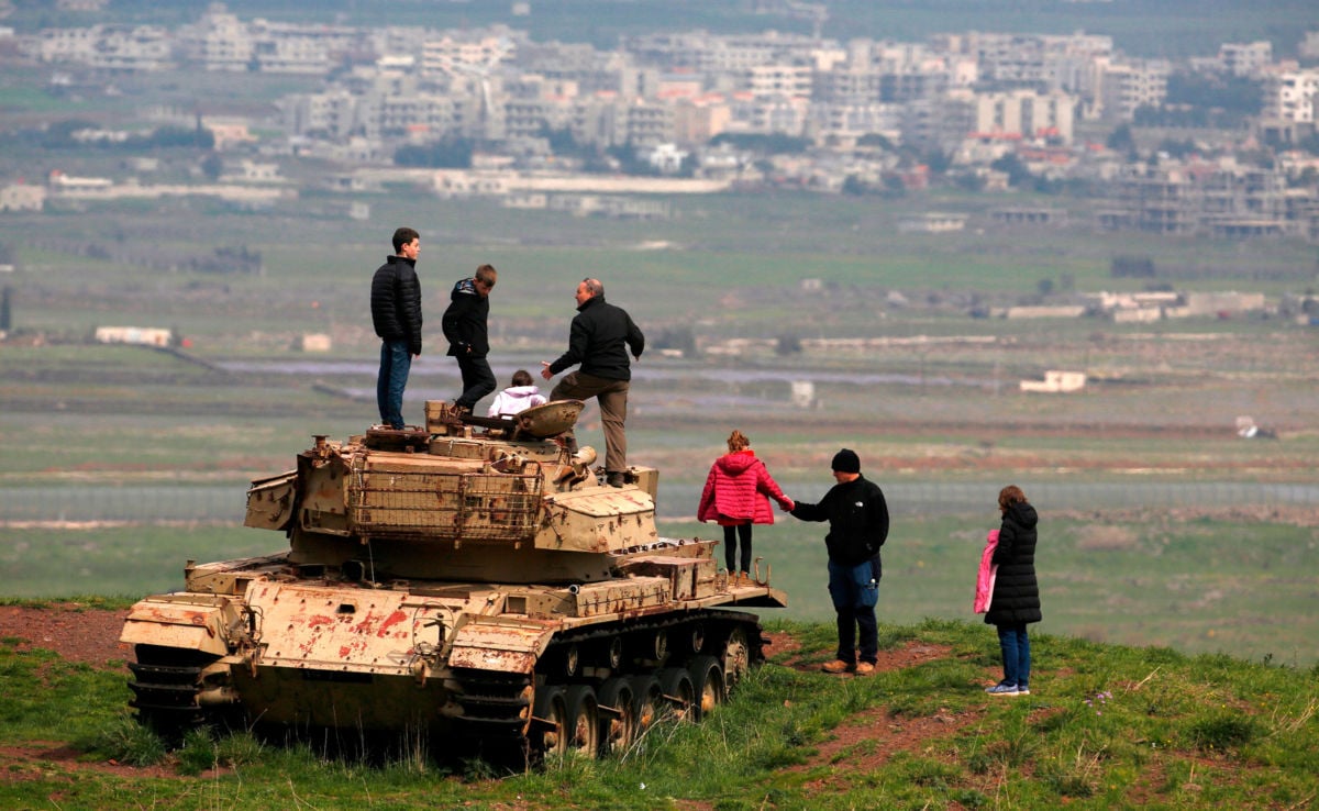 People stand on top of an old Israeli tank near the Israeli-Syrian border in the Israeli-annexed Golan Heights on March 23, 2019, facing the Syrian city of Qunaitra.