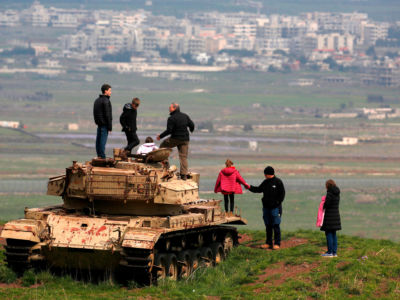 People stand on top of an old Israeli tank near the Israeli-Syrian border in the Israeli-annexed Golan Heights on March 23, 2019, facing the Syrian city of Qunaitra.