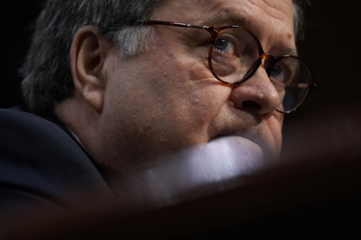 William Barr, a somewhat toadlike and bespectacled older man, is seen from below the edge of his desk