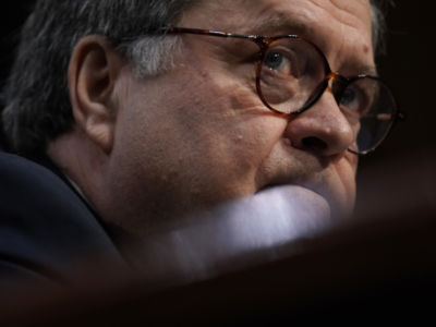 William Barr, a somewhat toadlike and bespectacled older man, is seen from below the edge of his desk