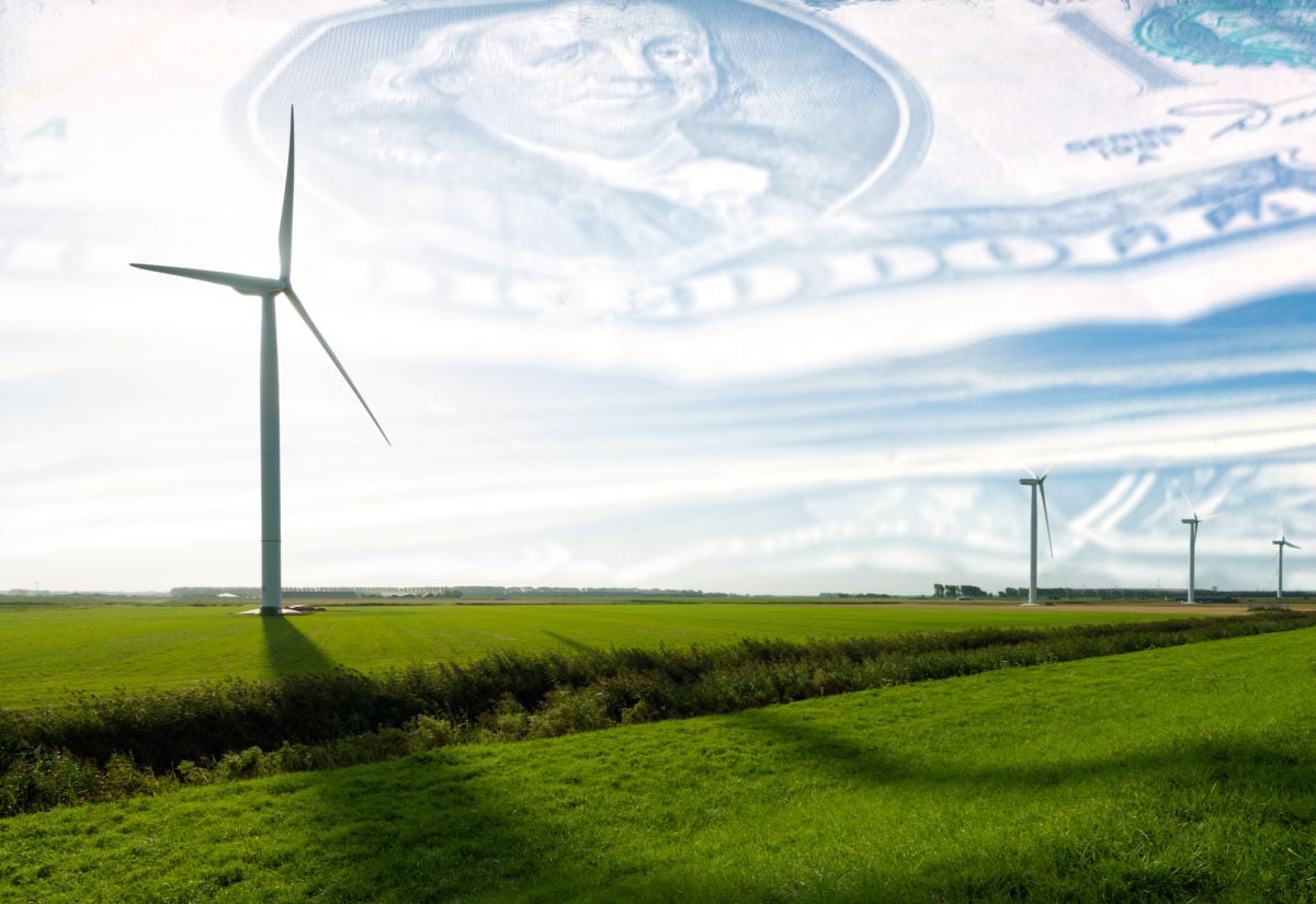 Wind turbines stand on green plains in front of a blue sky with a filter of U.S dollars