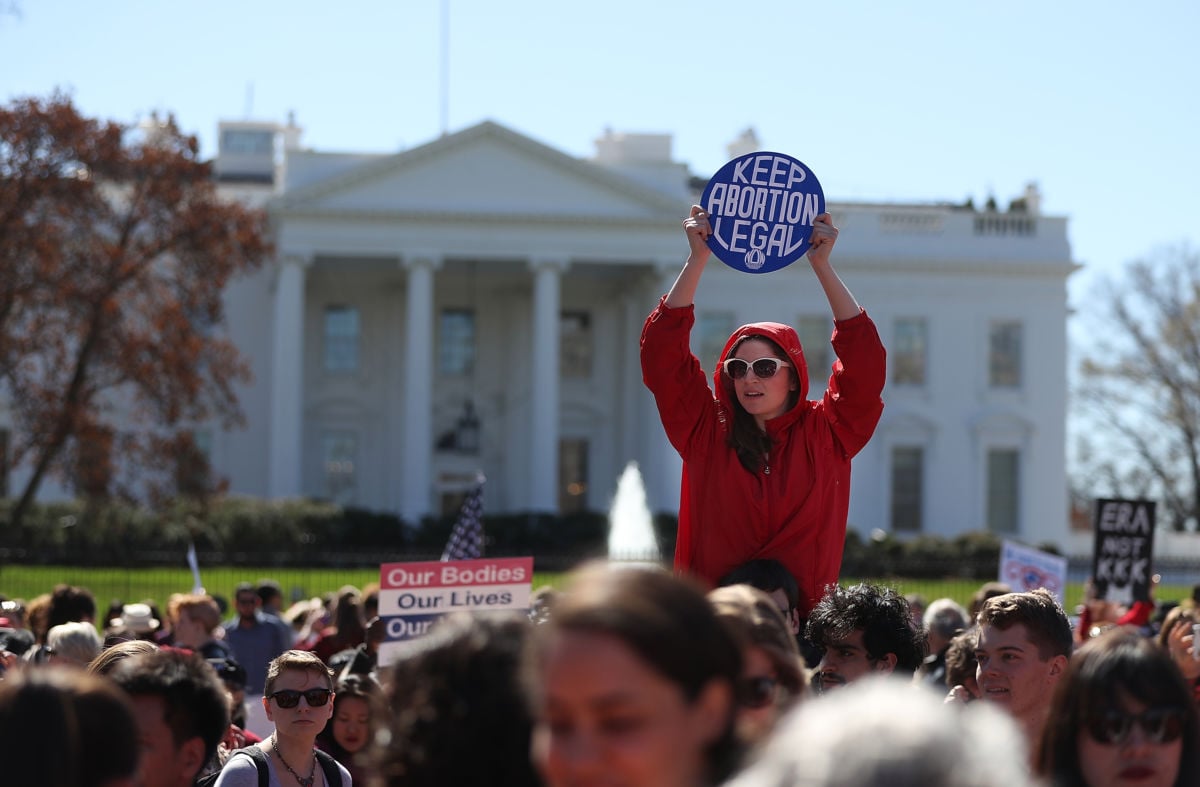 A woman in a red hoodie stands above a crowd holding a "Keep abortion legal" sign