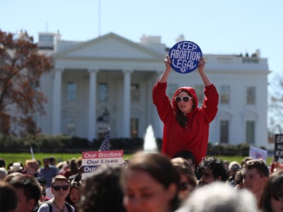 A woman in a red hoodie stands above a crowd holding a "Keep abortion legal" sign