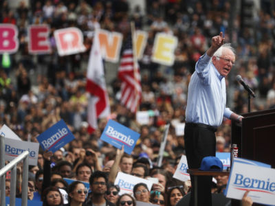 Bernie Sanders speaks at a podium surrounded by a huge crowd of supporters
