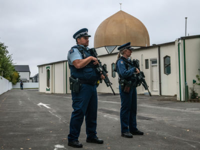 Two cops holding guns stand outside the golden domes of a mosque