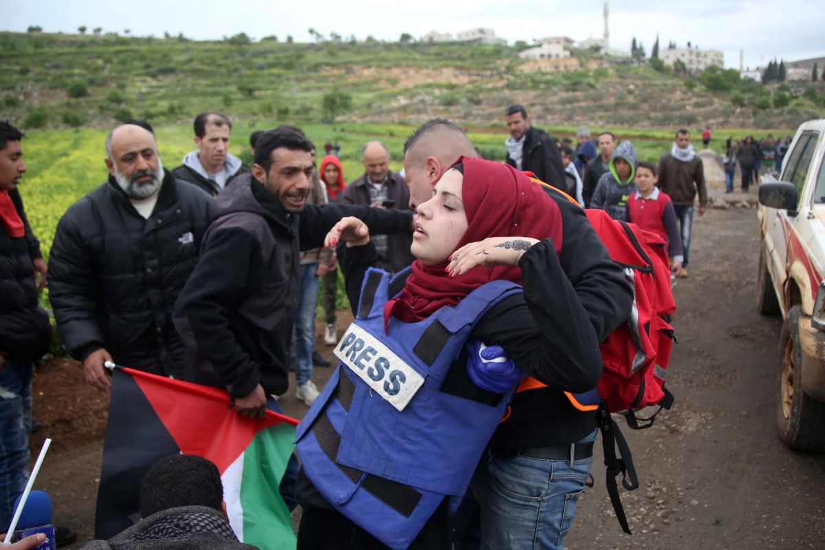 A wounded woman in a blue "PRESS" vest is carried away by men