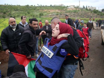 A wounded woman in a blue "PRESS" vest is carried away by men
