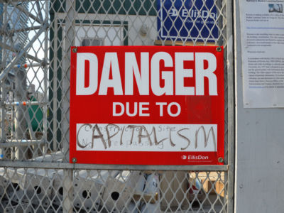 A sign posted on a construction site says, "Danger Due to Capitalism."