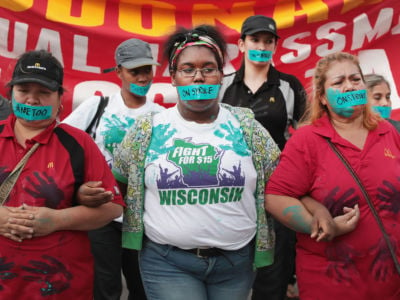 Women with blue tape over their mouths link arms during protest march