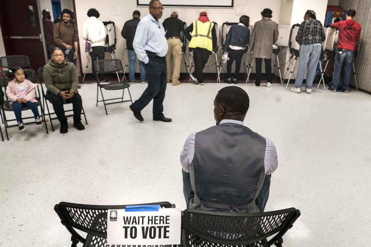 A Black man waits to vote as others stand in a line in front of him