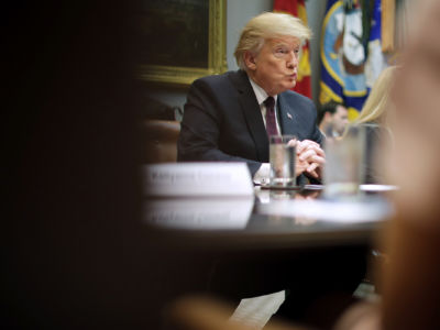 Donald Trump sits with folded hands and disheveled hair at a desk