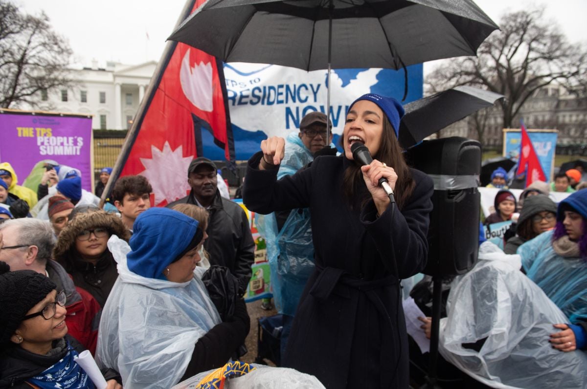 AOC speaks during an event in the rain, surrounded by supporters