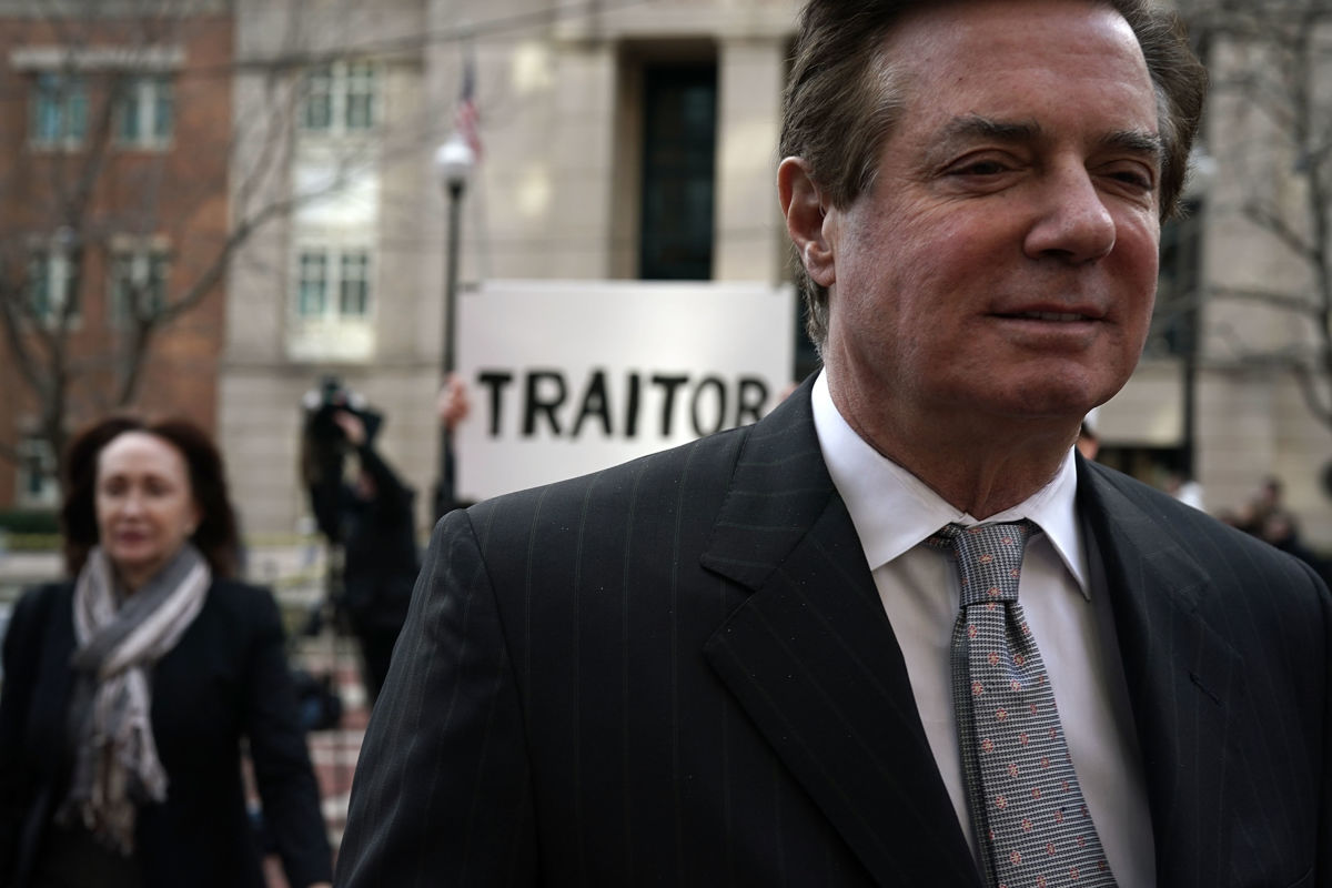 Paul Manafort walks away from man holding a sign reading "TRAITOR"