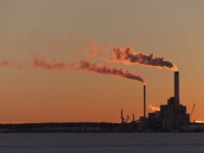 Smokestacks are backlit by a peach and orange sunset