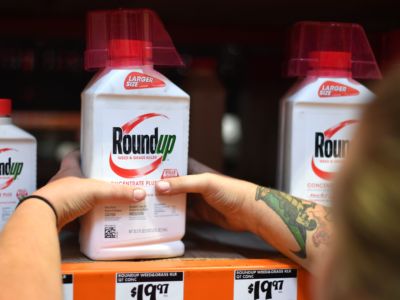 Tattooed hands grab a bottle of Roundup from a shelf