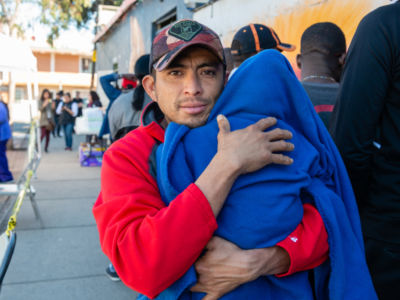 A man in a red sweater holds a child in a blue blanket