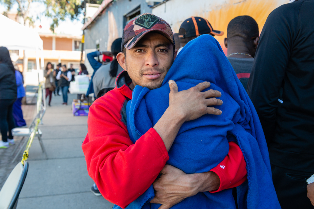 A man in a red sweater holds a child in a blue blanket