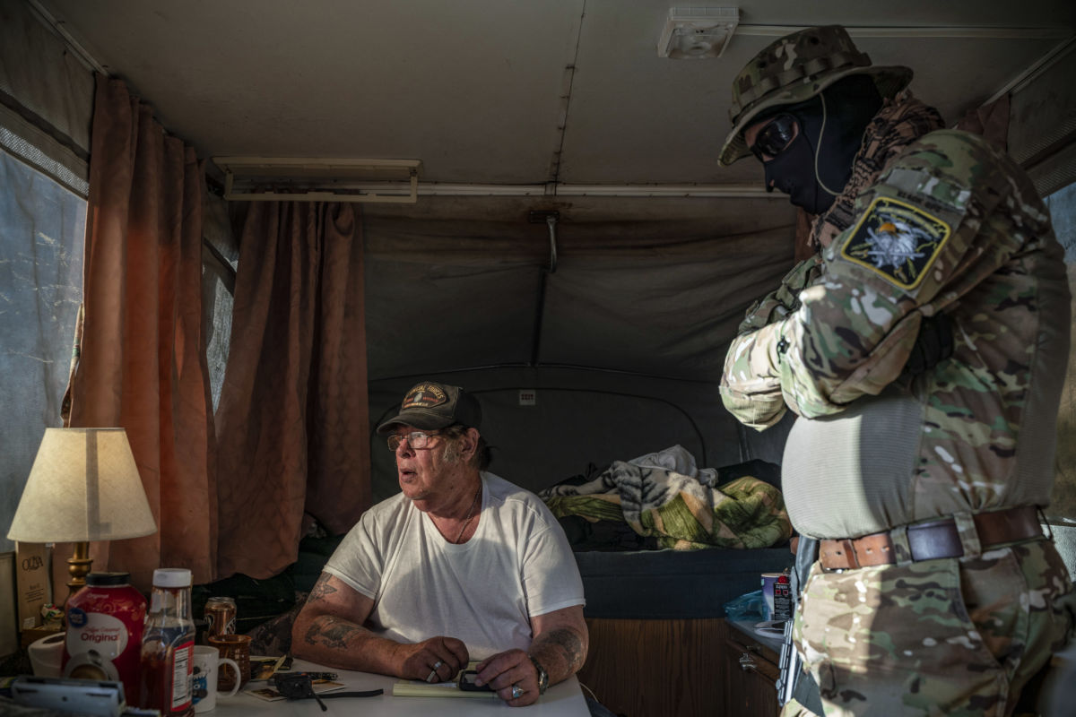 Two men sit speak to eachother while inside of a camper