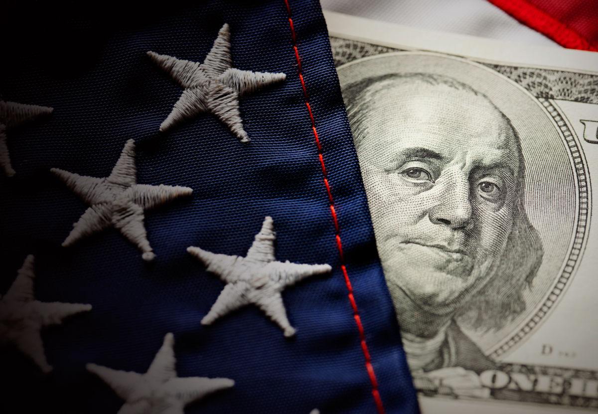 A hundred-dollar bill peeks out from behind a U.S. flag
