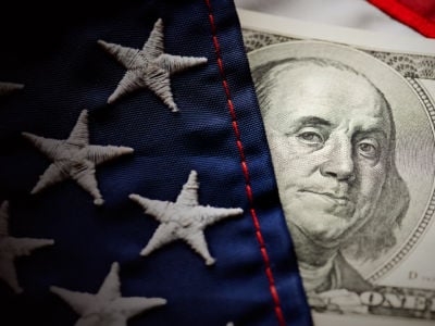 A hundred-dollar bill peeks out from behind a U.S. flag