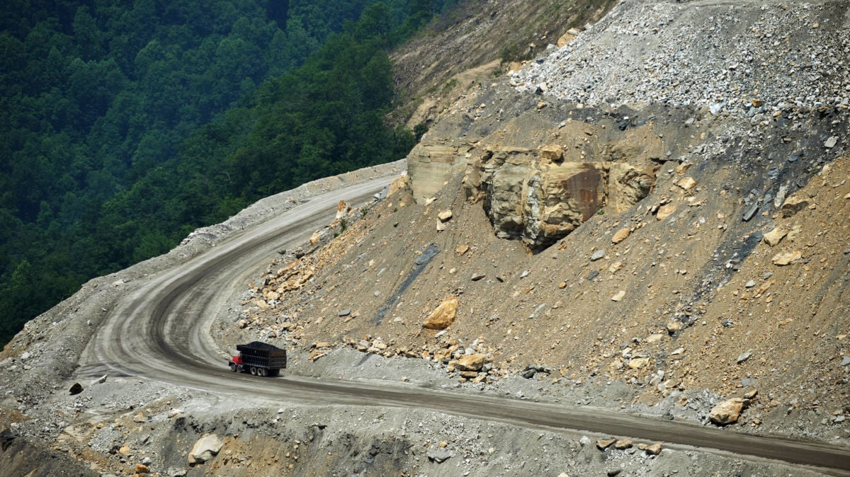 A dumptruck drives up a mined mountain as a forest is seen in the background