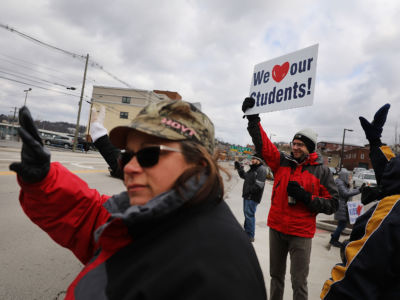 A man holds a sign reading "We [heart] our students!" during a demonstration